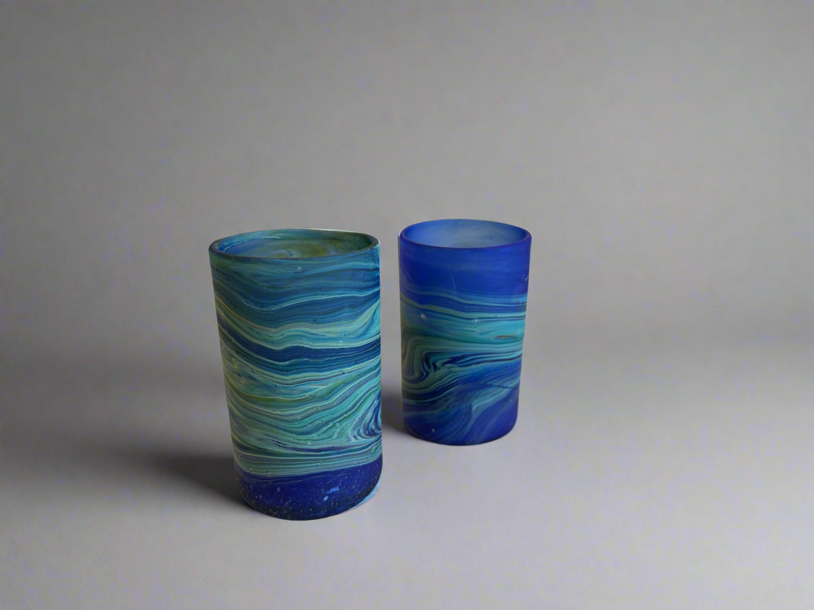Two blue and green marbled phoenician hebron glass tumblers on a plain background