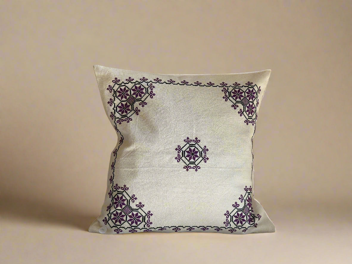 A square-shaped cushion cover with a geometric Canaanite star motif embroidered in purple on a beige background.